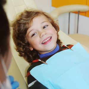 A cute, curly-haired child indulges and grimaces in a dental chair