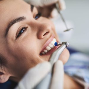 Close up portrait of pretty girl sitting in dental chair while stomatologist holding polisher and mirror. Girl is smiling